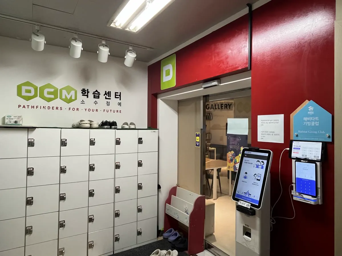 디씨엠학습센터 입구. 로고 벽 옆으로 클래스업 키오스크가 학생들을 맞아요.